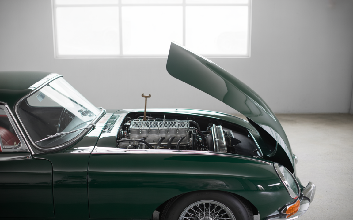 Voiture classique de sport verte avec le capot ouvert, révélant un moteur détaillé et une carrosserie brillante. Fond minimaliste.