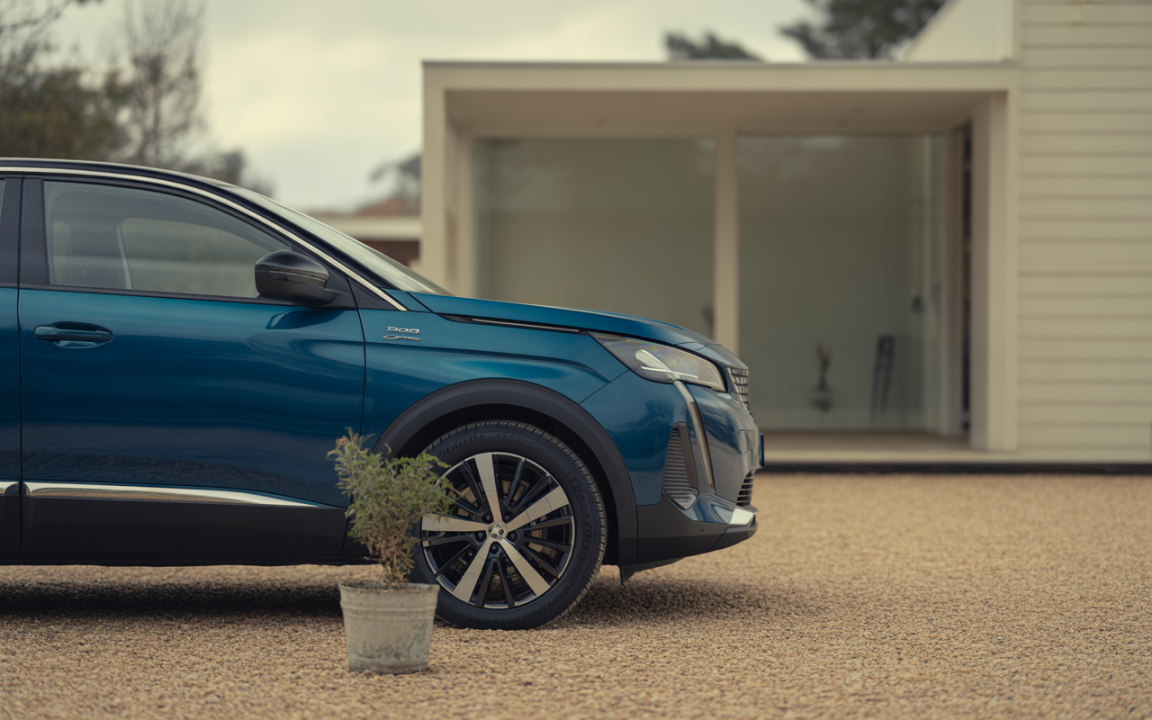 Voiture moderne bleu, vue de profil, stationnée devant une maison contemporaine, avec des cailloux et une plante en pot.