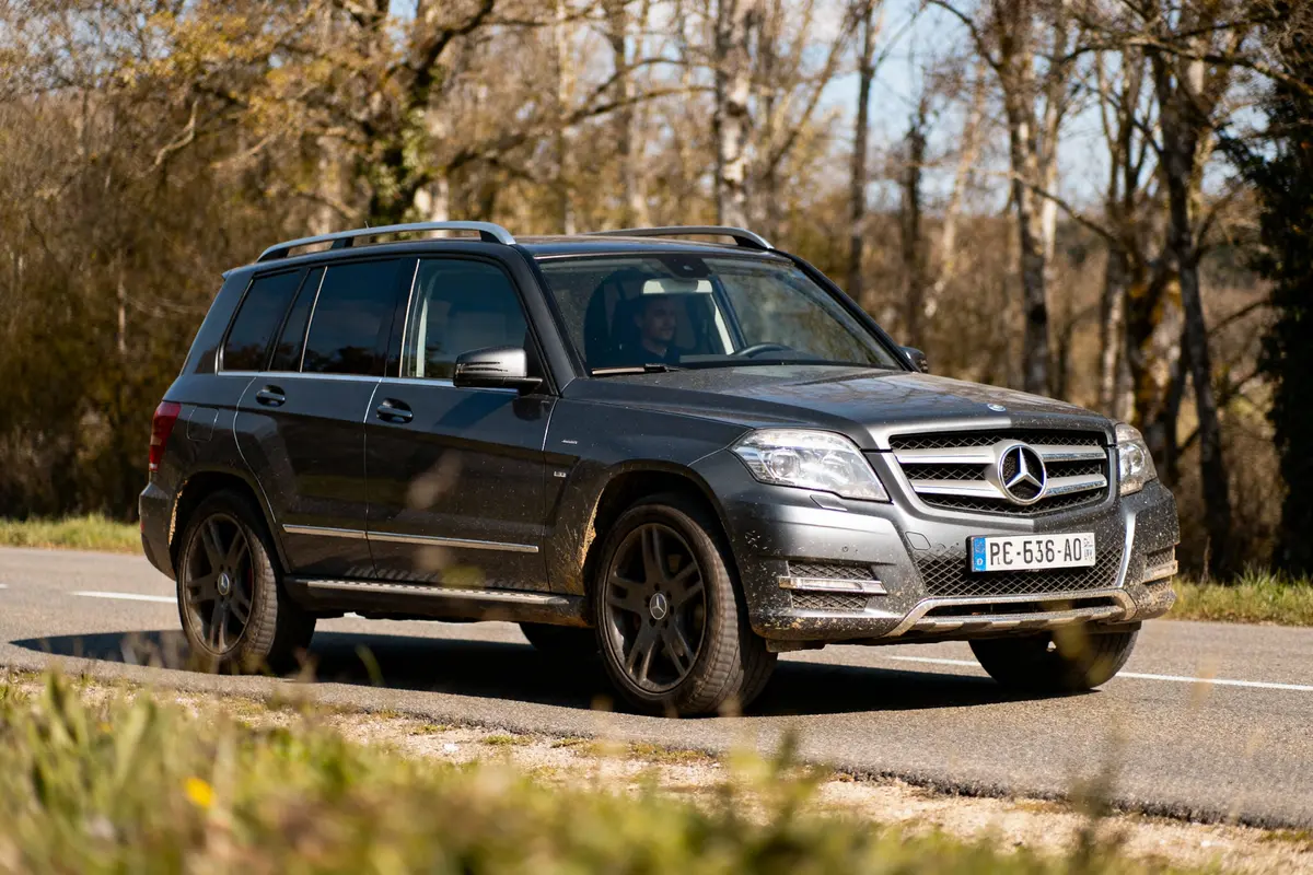 SUV Mercedes gris roulant sur une route, entouré d'arbres, par temps ensoleillé. Plaque d'immatriculation visible.