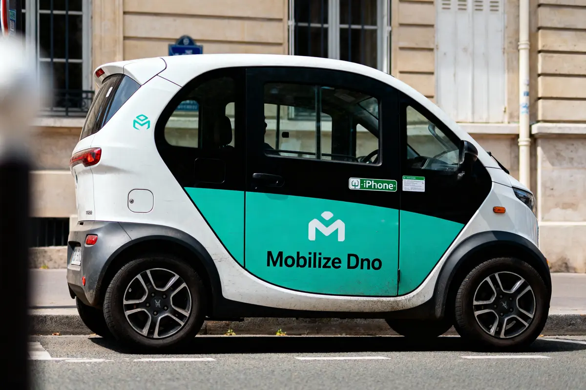 Petite voiture électrique "Mobilize Dno" blanche et verte stationnée devant un bâtiment.