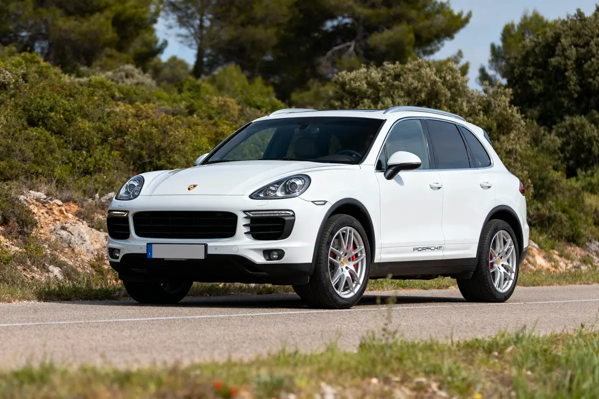 SUV blanc garé sur une route, entouré de végétation luxuriante sous un ciel bleu clair.