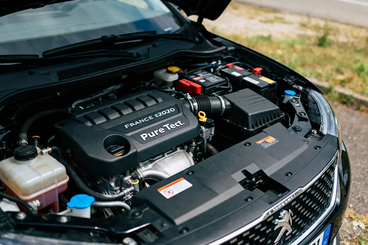 Moteur PureTech Peugeot sous le capot d'une voiture. Étiquettes lisibles, environnement extérieur visible.