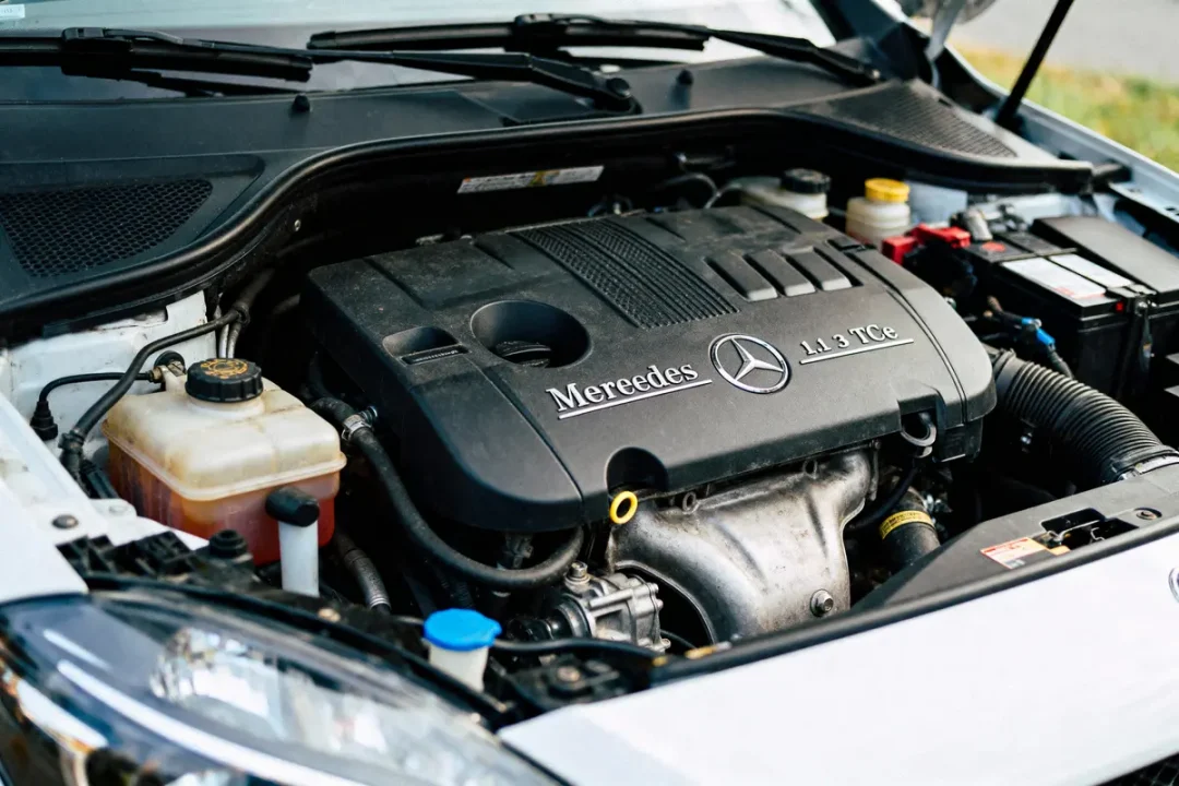 Moteur de voiture sous capot ouvert avec logo et texte "Mereedes 1.3 TCe" visibles en gros plan.