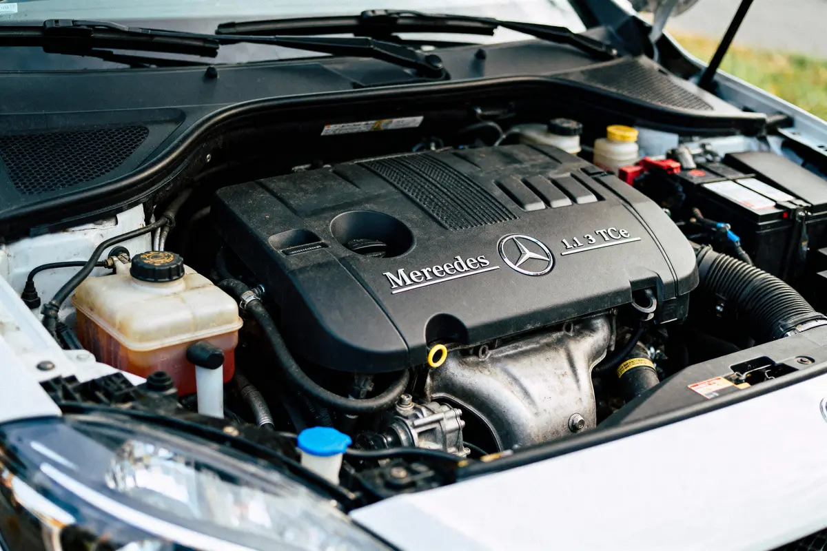 Moteur de voiture sous capot ouvert avec logo et texte "Mereedes 1.3 TCe" visibles en gros plan.