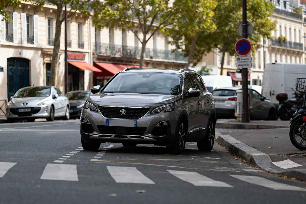 SUV Peugeot gris stationné en ville près d'un trottoir, entouré d'autres voitures et bâtiments urbains.