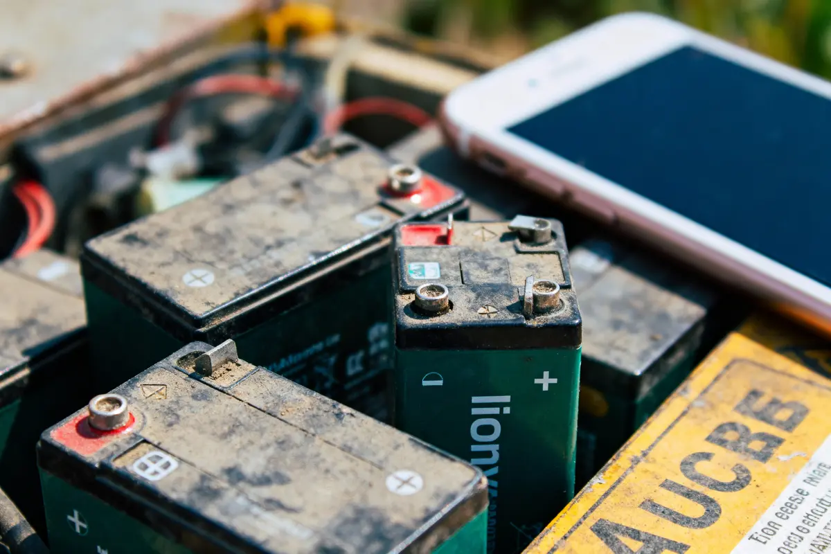 Vieilles batteries usagées avec un smartphone blanc posé à côté, sur une surface poussiéreuse.