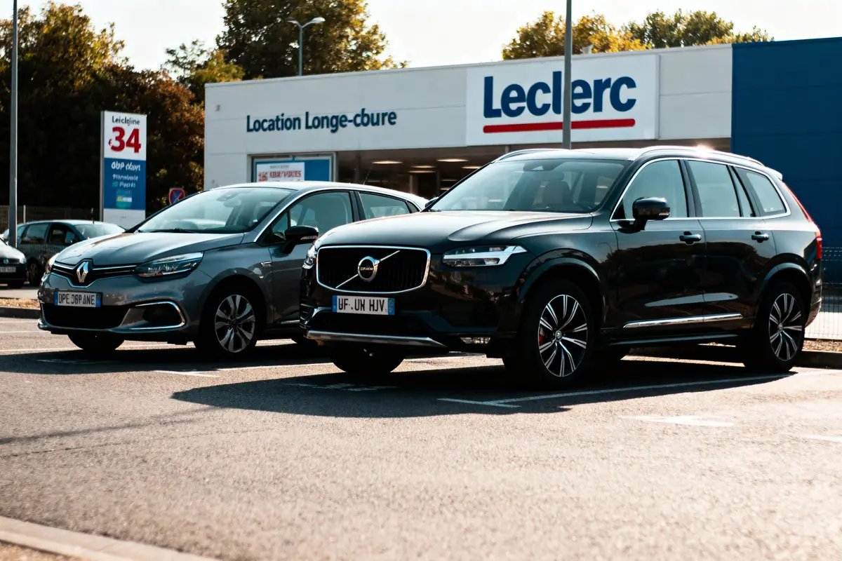Deux voitures garées devant une enseigne Leclerc, stationnement ensoleillé.