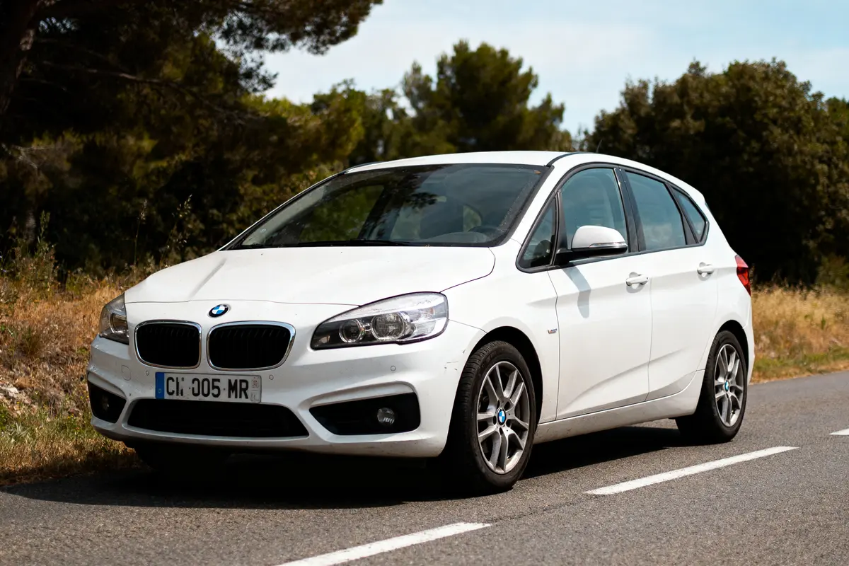 Voiture blanche garée sur une route, entourée d'arbres et de buissons en arrière-plan.