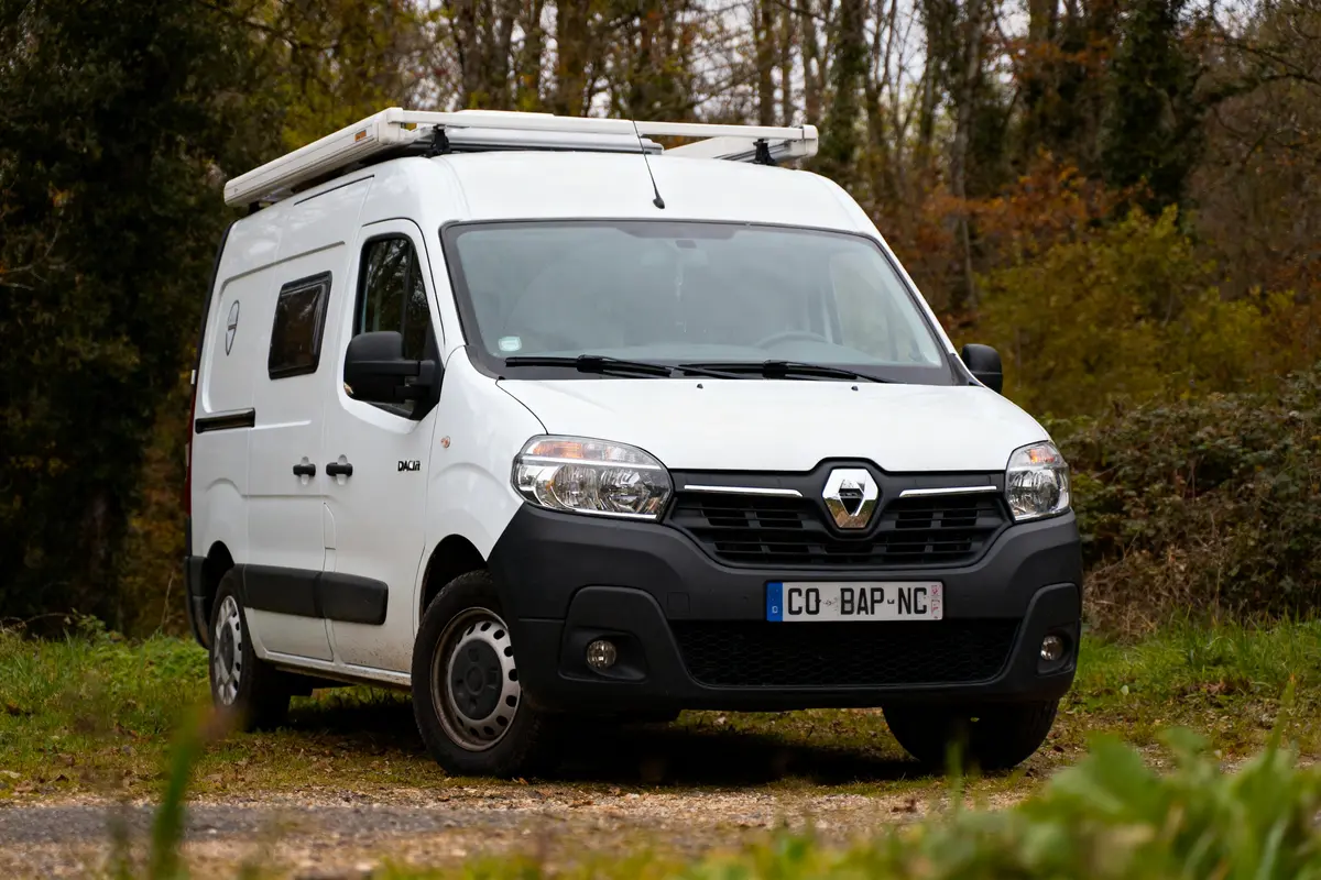 Fourgon blanc Renault dans un cadre forestier automnal, parcé sur un chemin herbu.