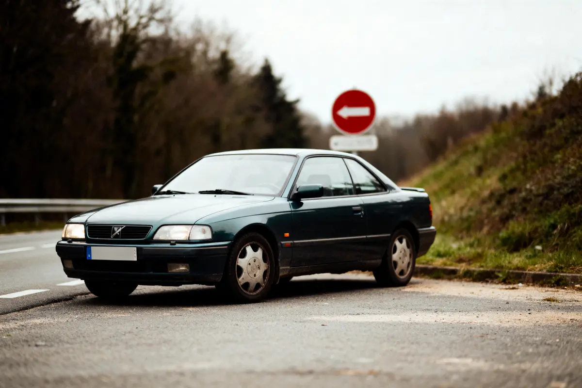 Voiture verte ancienne garée au bord de la route avec panneau sens interdit en arrière-plan.