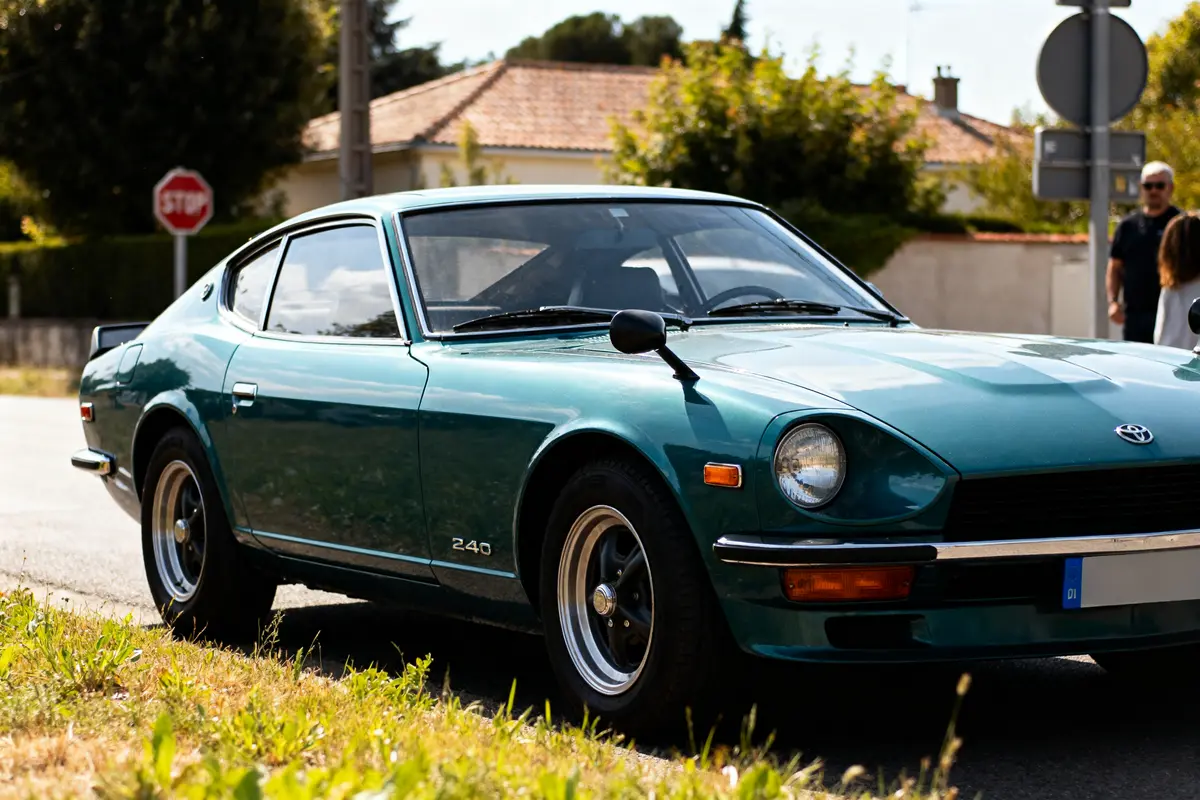 Voiture classique Datsun 240z automatic verte garée sur route ensoleillée devant maison.