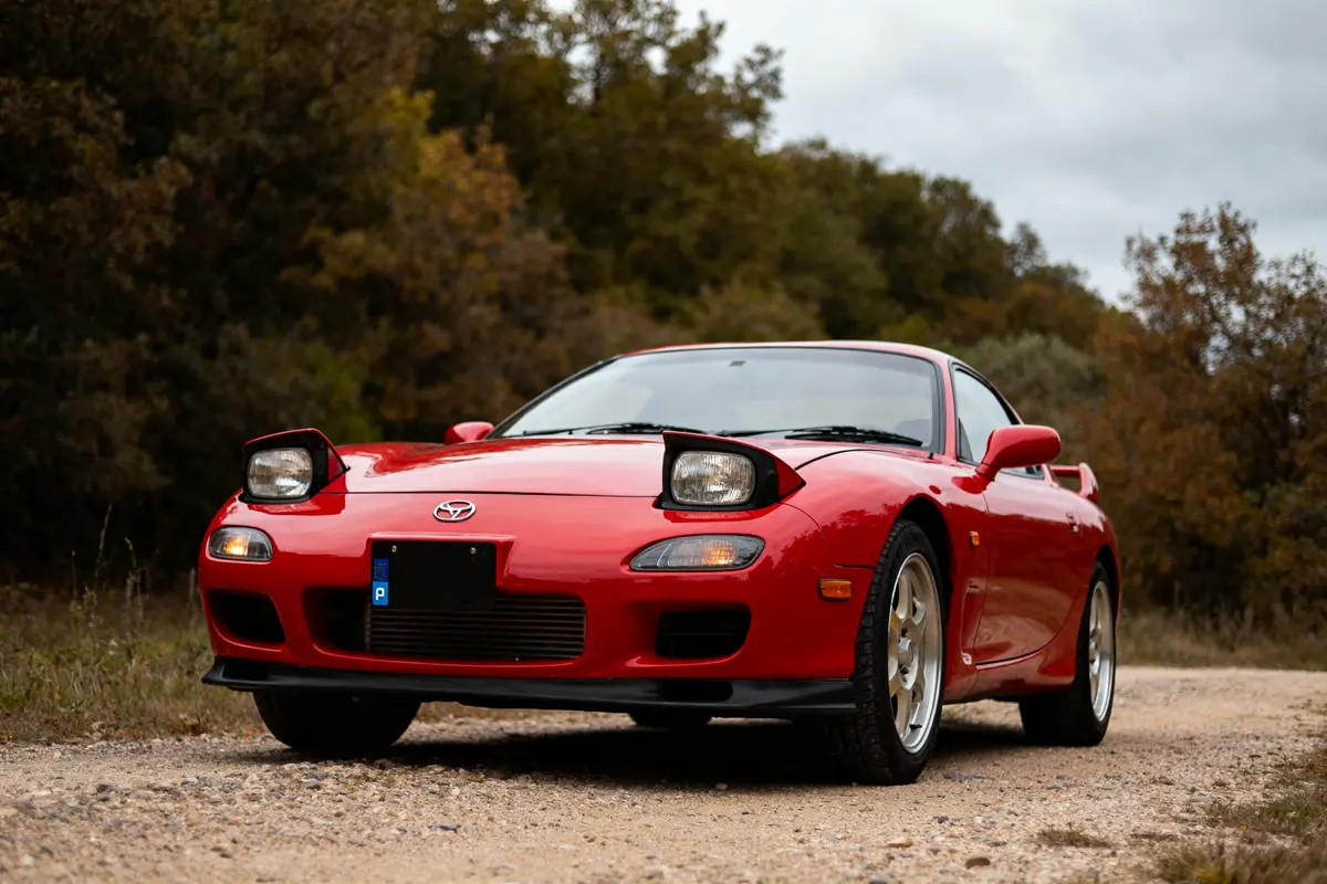 Voiture sportive rouge Mazda RX7 coupé avec phares escamotables sur route de campagne