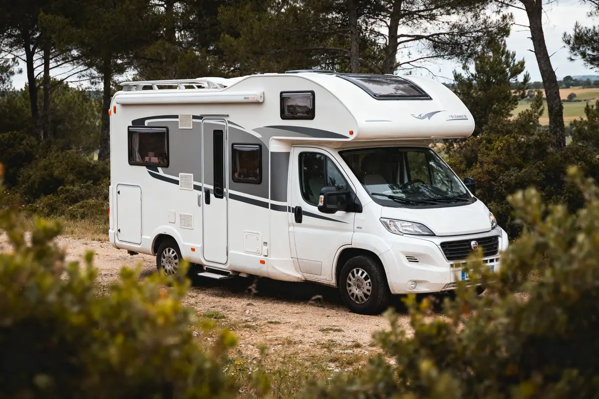 Camping-car blanc stationné en pleine nature, entouré d'arbres et de feuillage.
