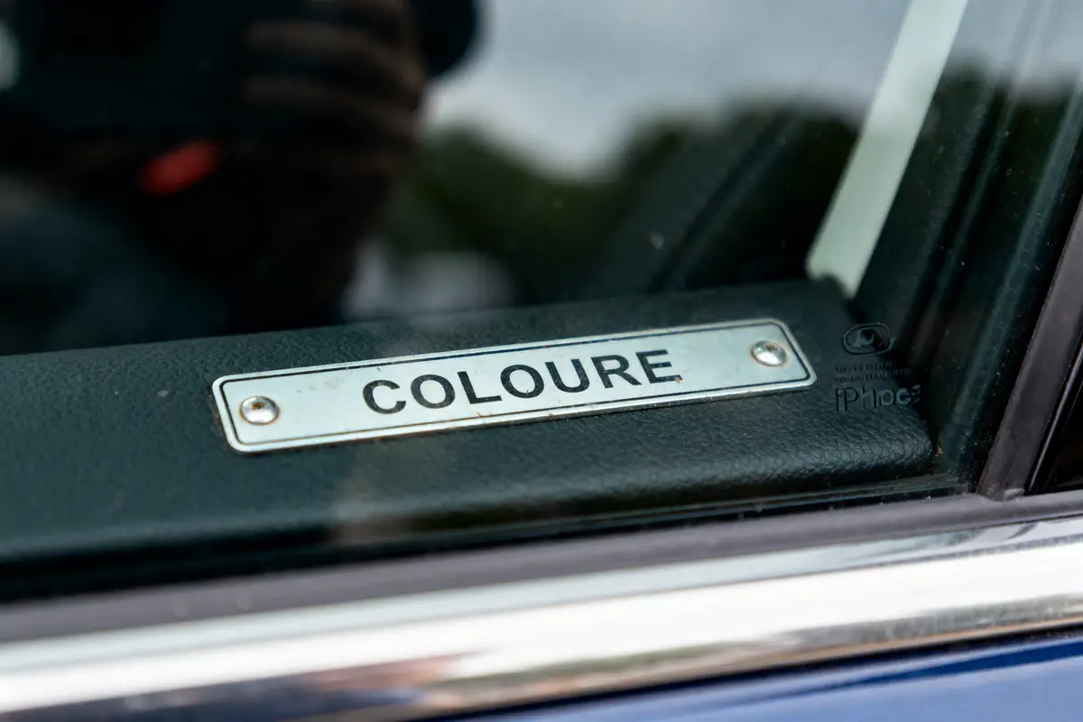 Plaque métallique avec inscription "COLOURE" en gros plan sur une surface en cuir noir.
