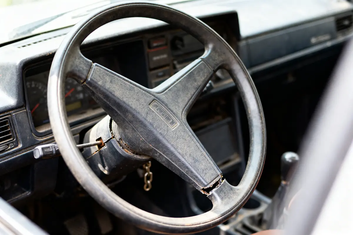 Volant d'une ancienne voiture avec tableau de bord décoloré et usé, intérieur rétro.