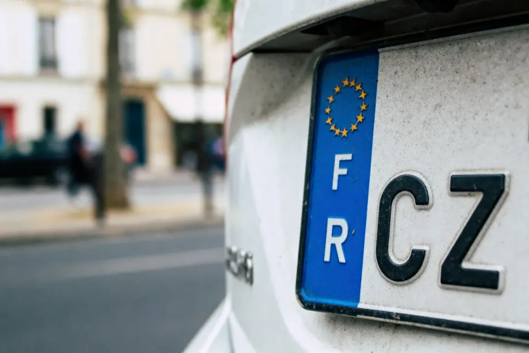Plaque d'immatriculation française avec symbole européen, voiture blanche sur rue floue en arrière-plan.