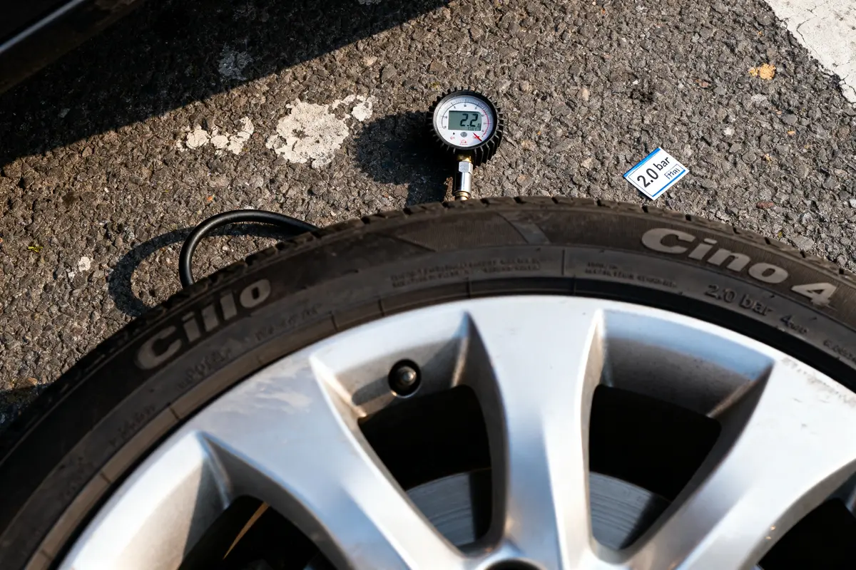 Pneu de voiture avec manomètre lisant 2,2 bars sur asphalte, étiquette "2.0 bar" visible.