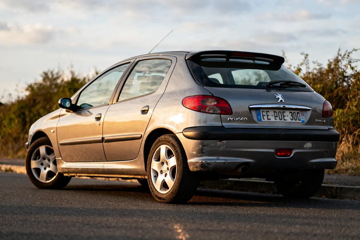 Voiture grise Peugeot 306 phase 2 garée sur une route au coucher du soleil