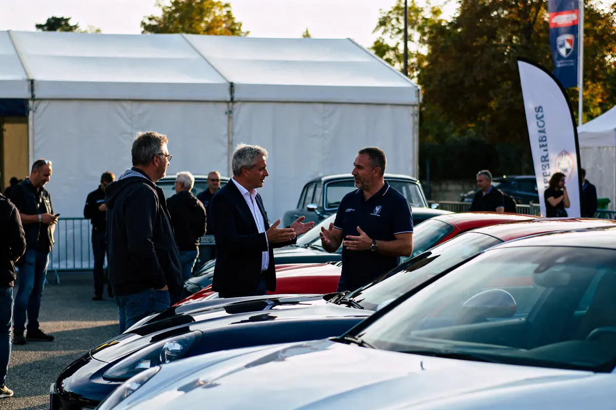 Des personnes discutent autour de voitures exposées lors d'un événement Motor1 en plein air