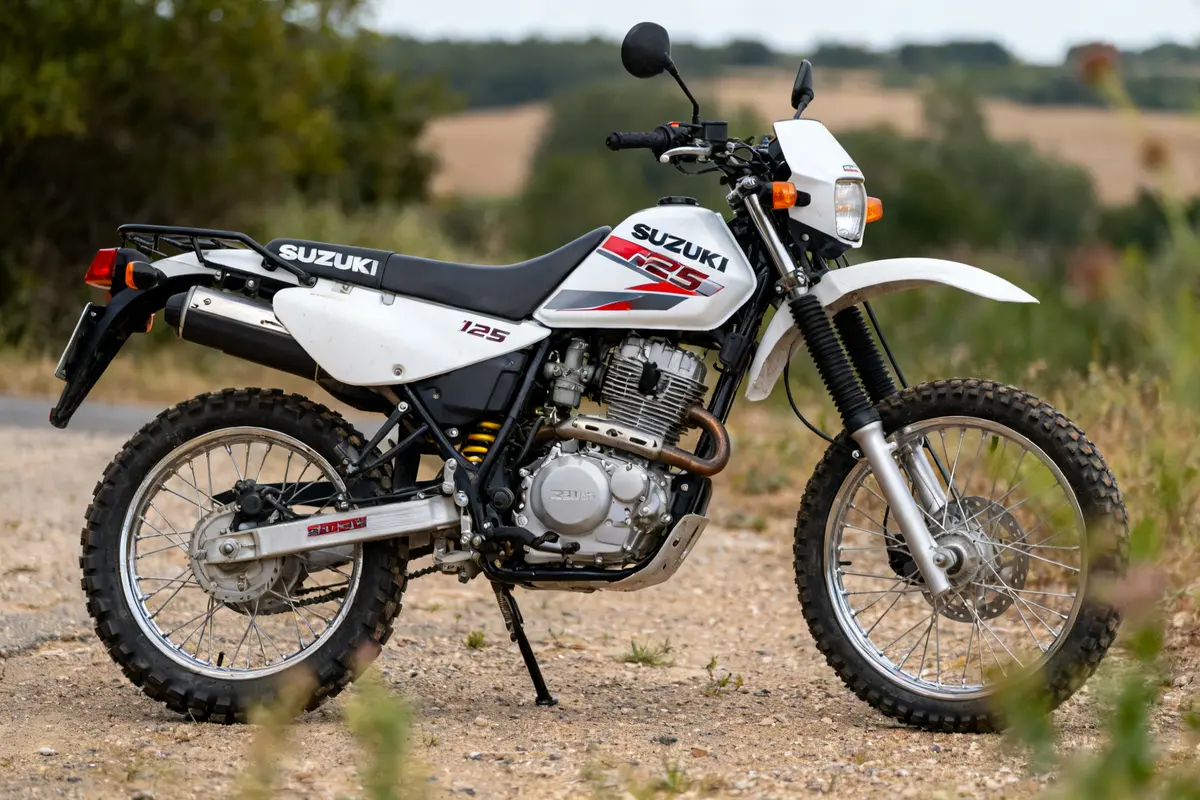 Moto tout-terrain blanche Suzuki Cross 125 stationnée sur un chemin de terre