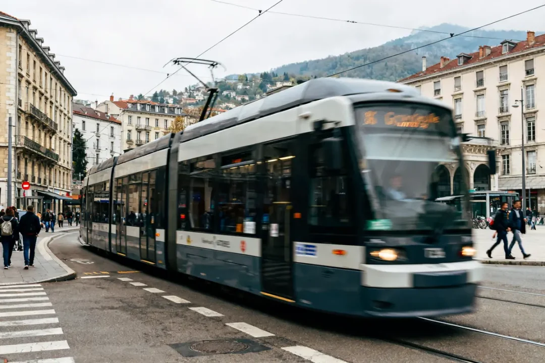 Tram D Grenoble passant dans une rue animée près de bâtiments historiques et collines environnantes