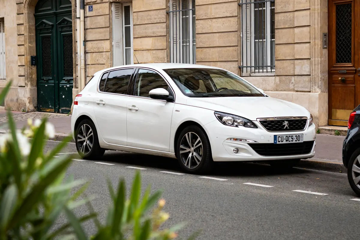 Voiture 308 blanche garée dans une rue parisienne près d'un immeuble haussmannien