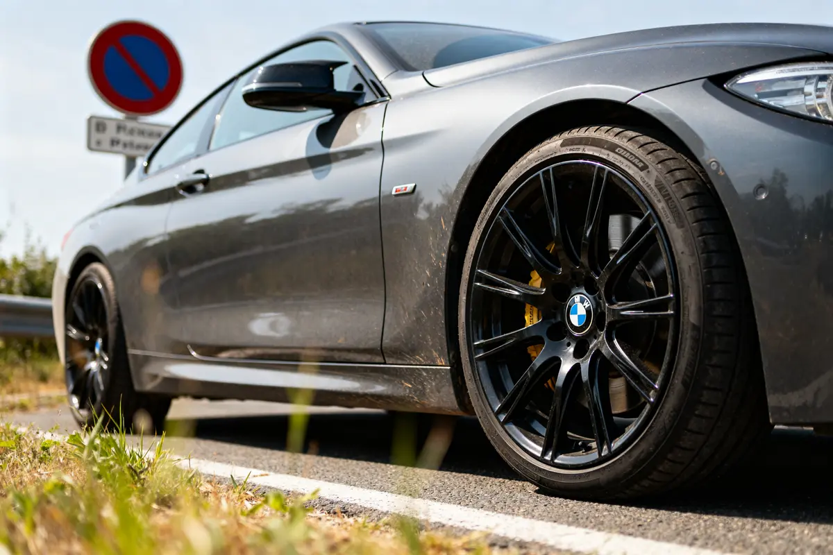 Voiture BMW grise avec jantes noires stationnée près d'un panneau d'interdiction.
