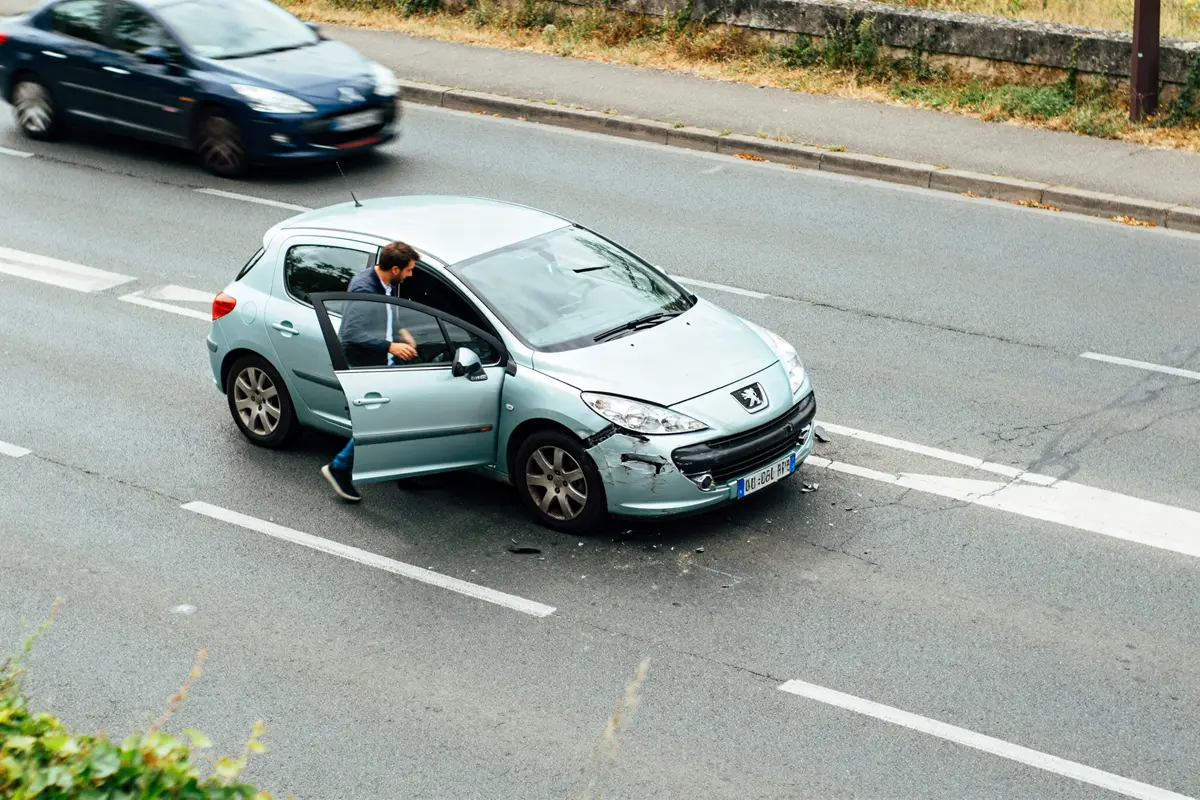 Conducteur inspectant une Peugeot 307 après un accrochage mineur et délit de fuite possible