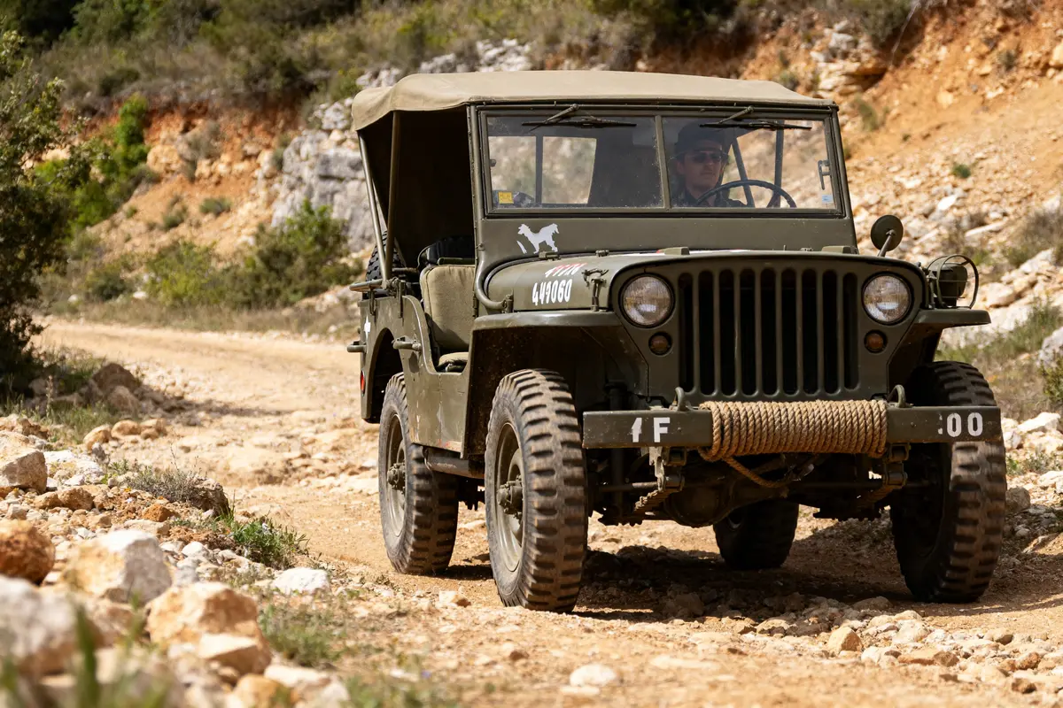 Jeep militaire roulant sur un chemin rocailleux en pleine nature avec un conducteur vigilant