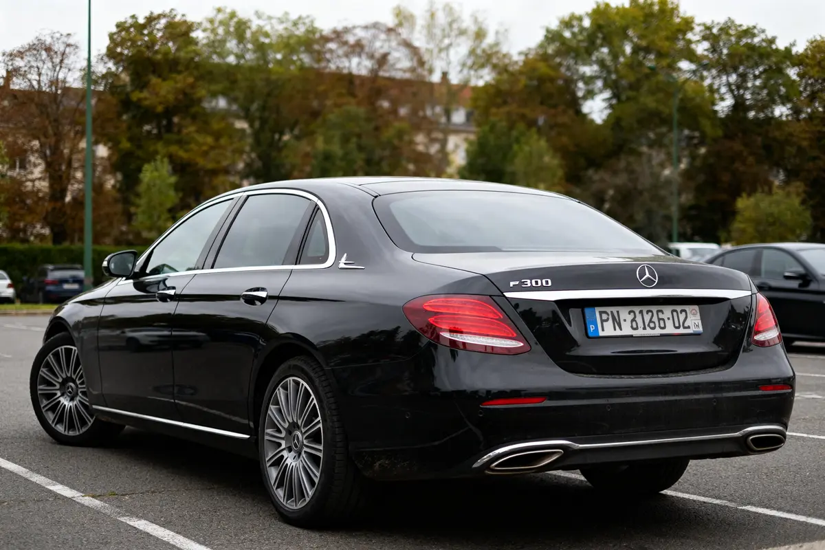 Vue arrière d'une Mercedes E 300 noire stationnée dans un parking extérieur.