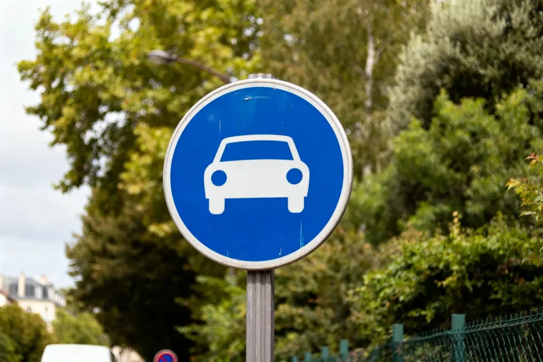 Panneau de signalisation rond indiquant une voie réservée voitures en fond de verdure.