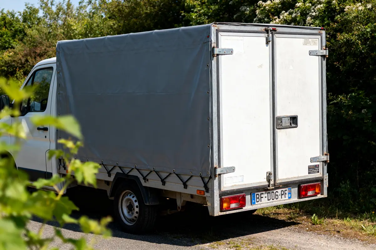 Camionnette blanche avec remorque fermée d'occasion garée sur une route entourée de verdure