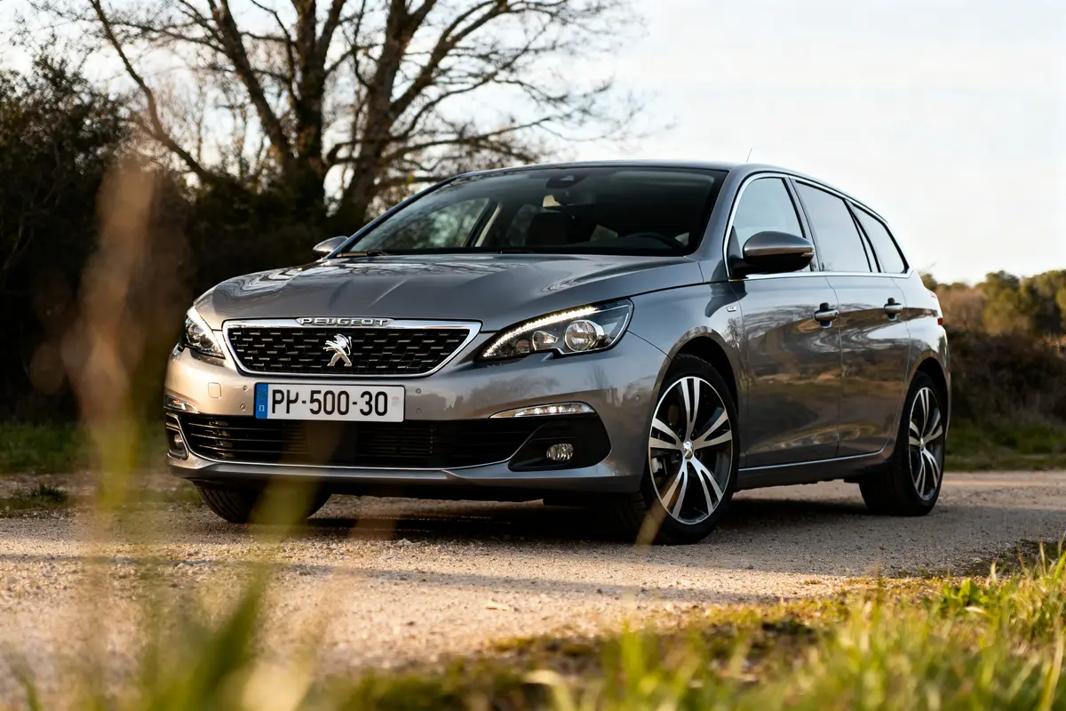 Voiture Peugeot 308 grise stationnée sur un chemin ensoleillé devant des arbres