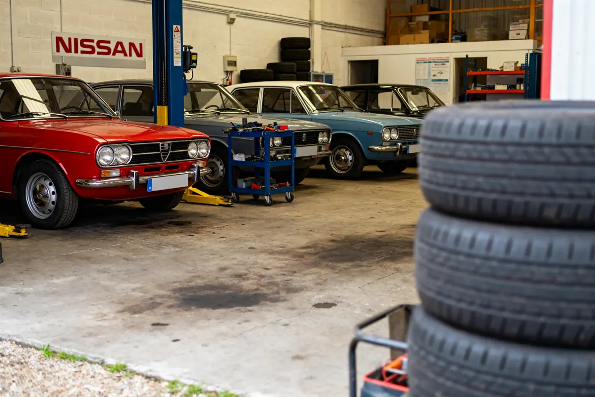 Voitures anciennes dans un atelier du garage Nissan à Chambourcy avec pneus empilés.