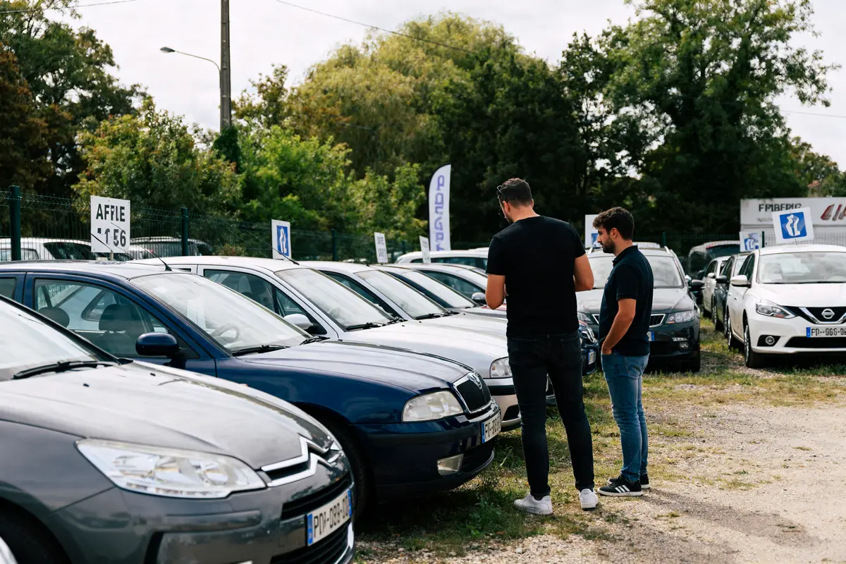 Deux hommes discutent devant des voitures d'occasion en vente sur moteurmag.com